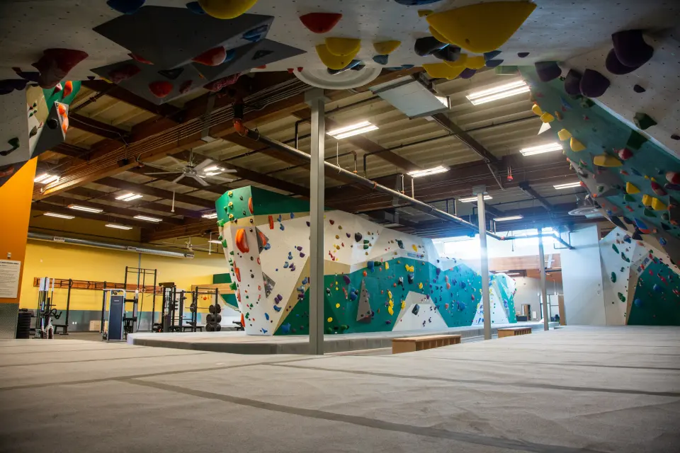 Teal and white bouldering walls on grey matting, with the weights area against a yellow wall