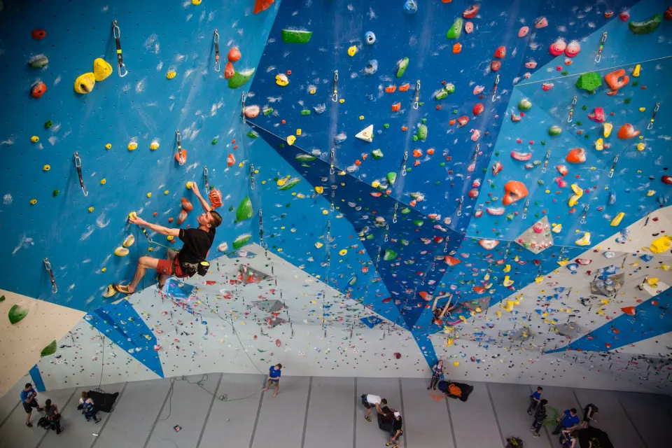 Lead climber high on a tall blue wall lined with quickdraws