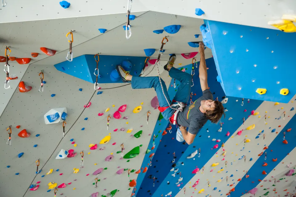 Lead climber clipping under a blue roof on the grey sport wall