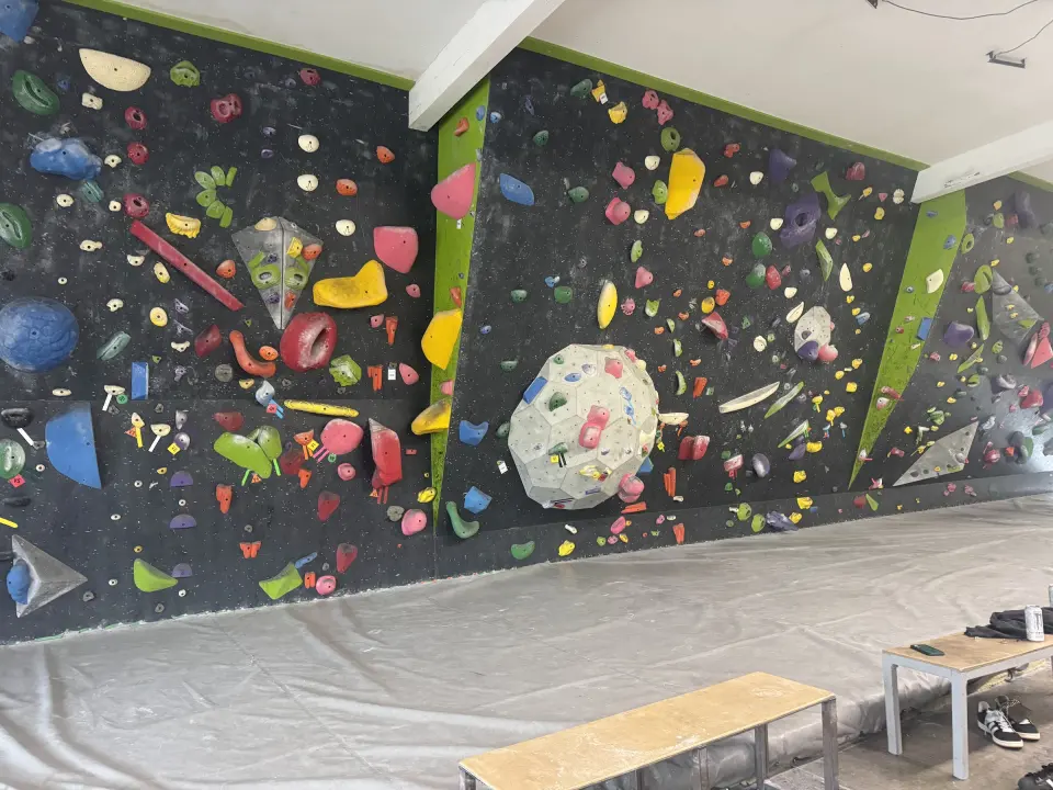 Black bouldering walls with lime-green trim above grey matting