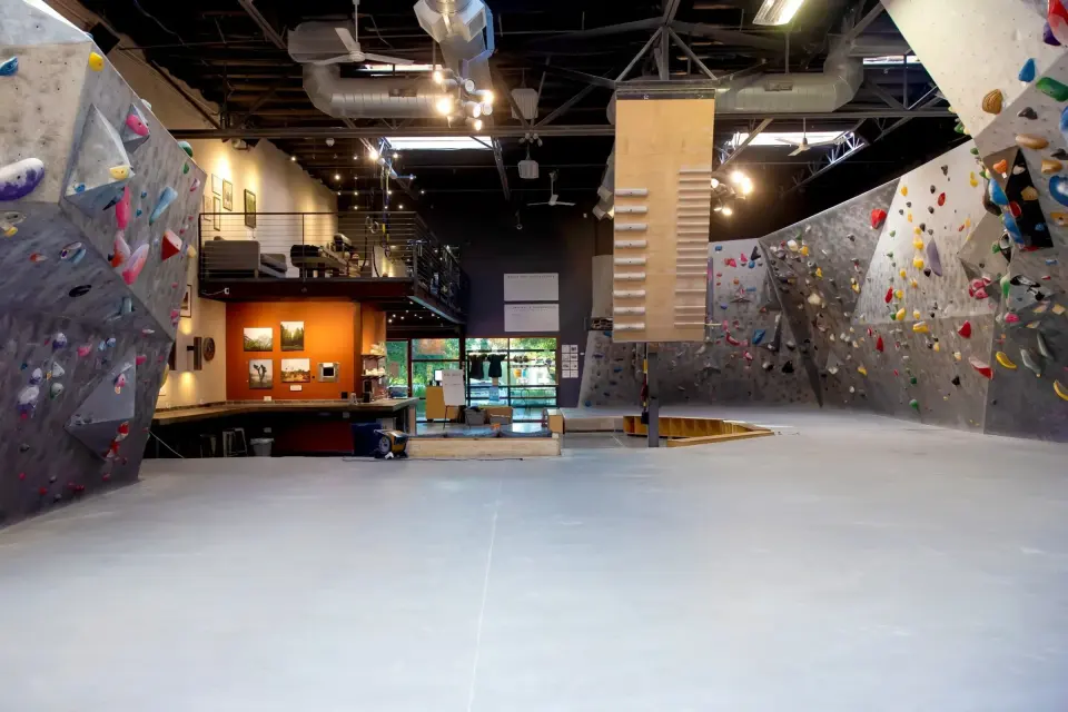 Bouldering walls around the open matted floor, with the hanging campus board and mezzanine