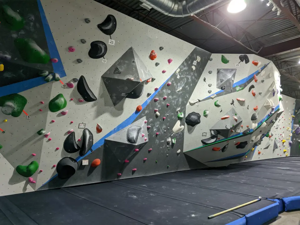 Long bouldering wall with grey volumes and a blue stripe