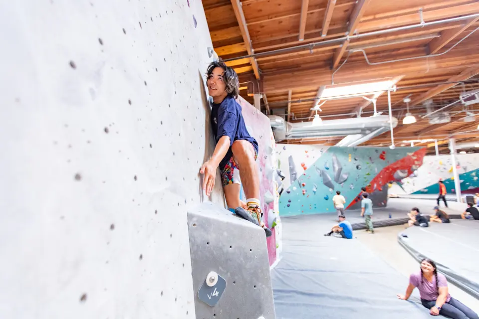 Climber on a vertical wall with the bouldering hall behind