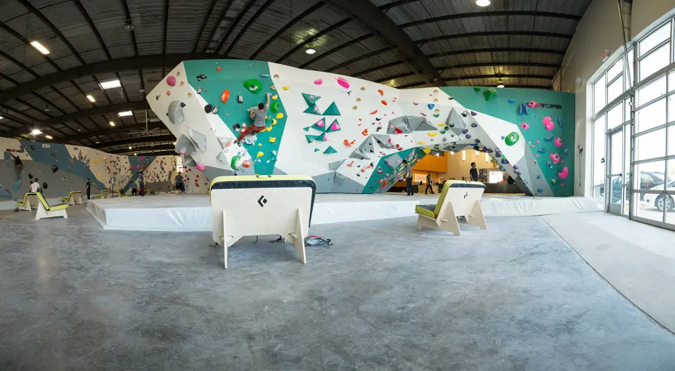 Wide view of the bouldering hall, with a long teal and white boulder under a warehouse roof