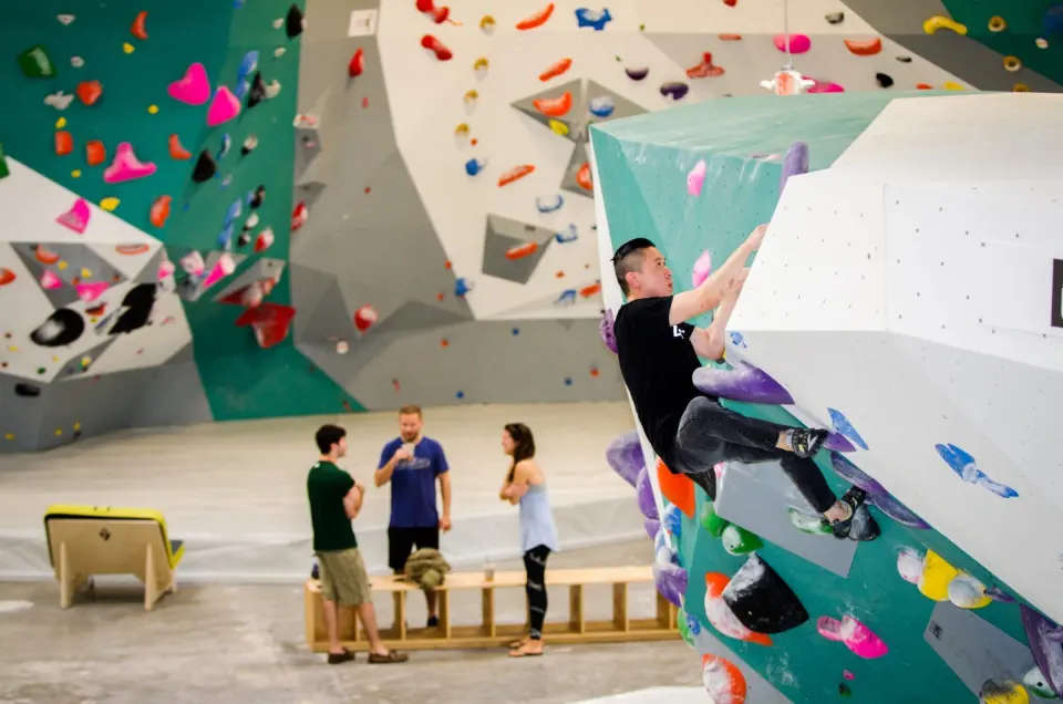 Climber on a teal and white boulder in front of a grey overhanging wall