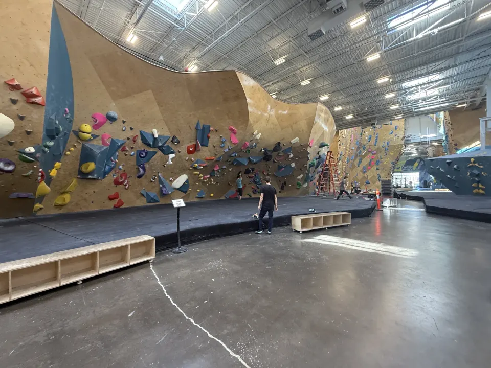 Long curving bouldering wall with blue volumes and a padded floor