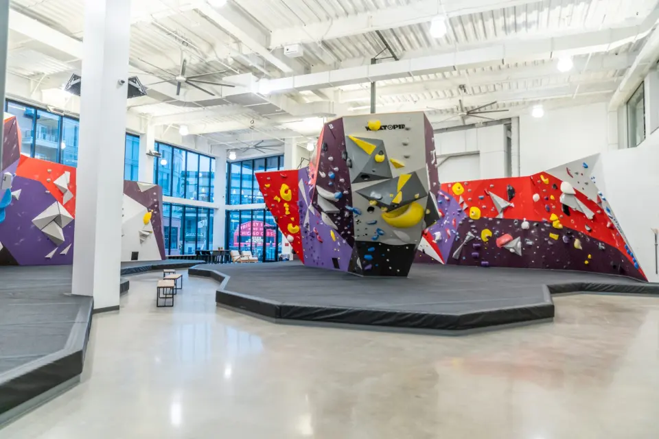 Bouldering hall with a central boulder and padded floor under big windows