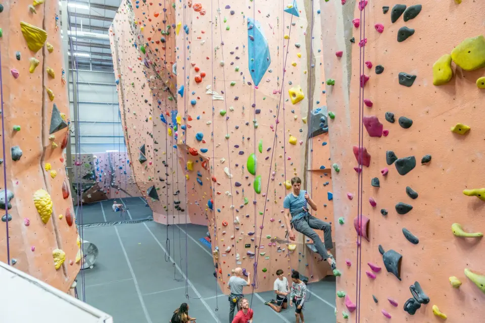 Tall peach-coloured rope walls with climbers on top-rope and lead