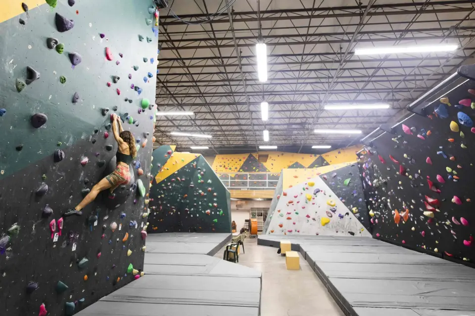 Climber on a teal wall looking down the length of the bouldering hall