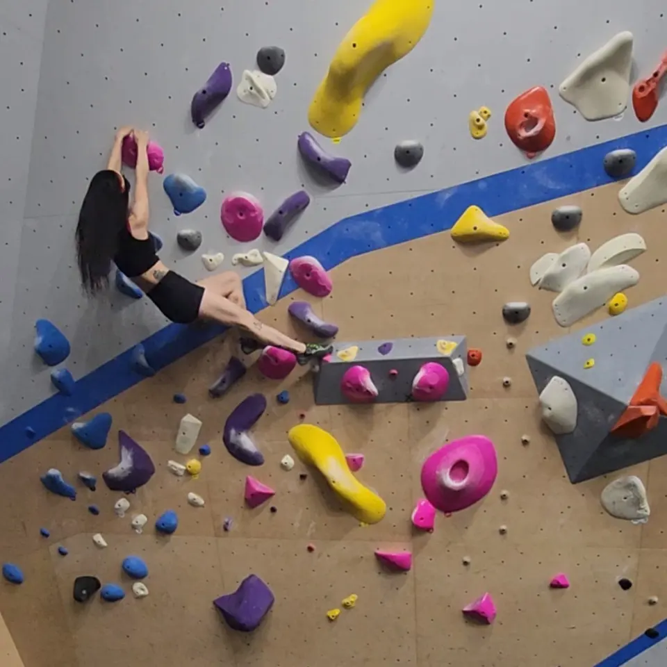 Climber stretching across a wall of pink, yellow and purple holds