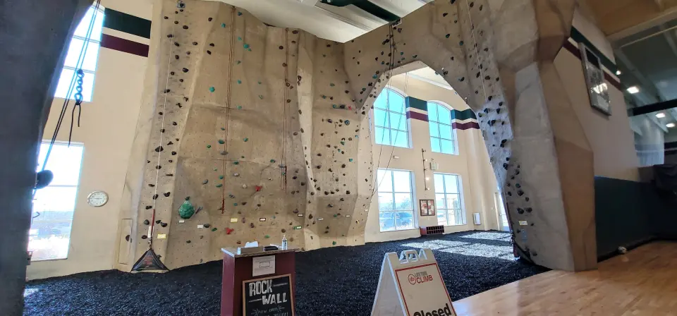 Sculpted beige rock wall with top ropes and a walk-through arch above a rubber-mulch floor