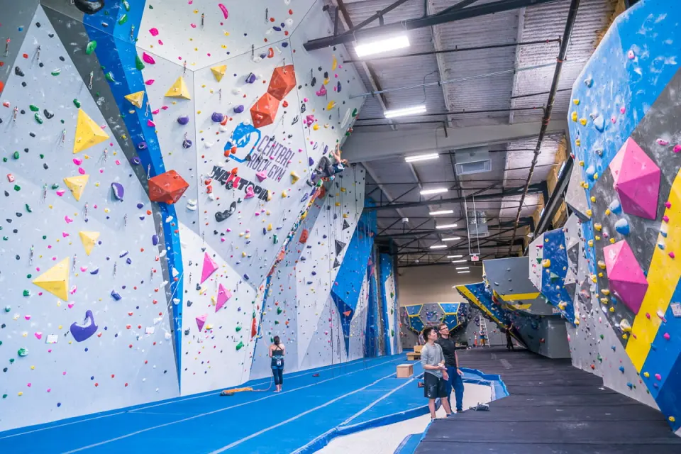 Long hall of roped walls with a lead climber, bouldering walls opposite