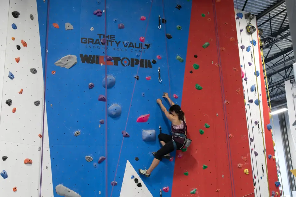 Climber on a blue top-rope wall below the Gravity Vault logo