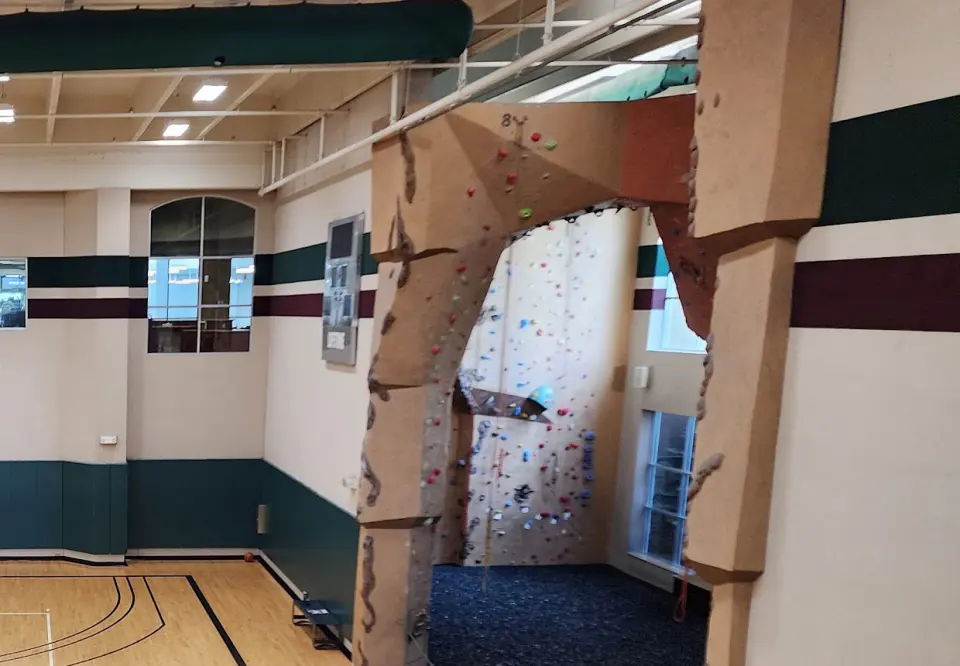 Sculpted rock arch and hold-covered climbing wall at the end of the gymnasium