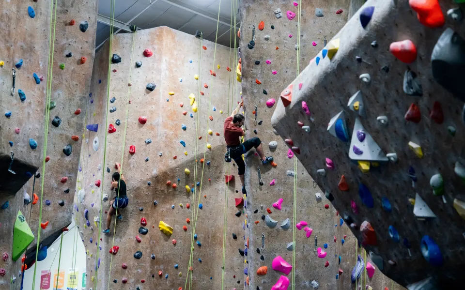 Climbers on tall top-rope walls beside an angled prow