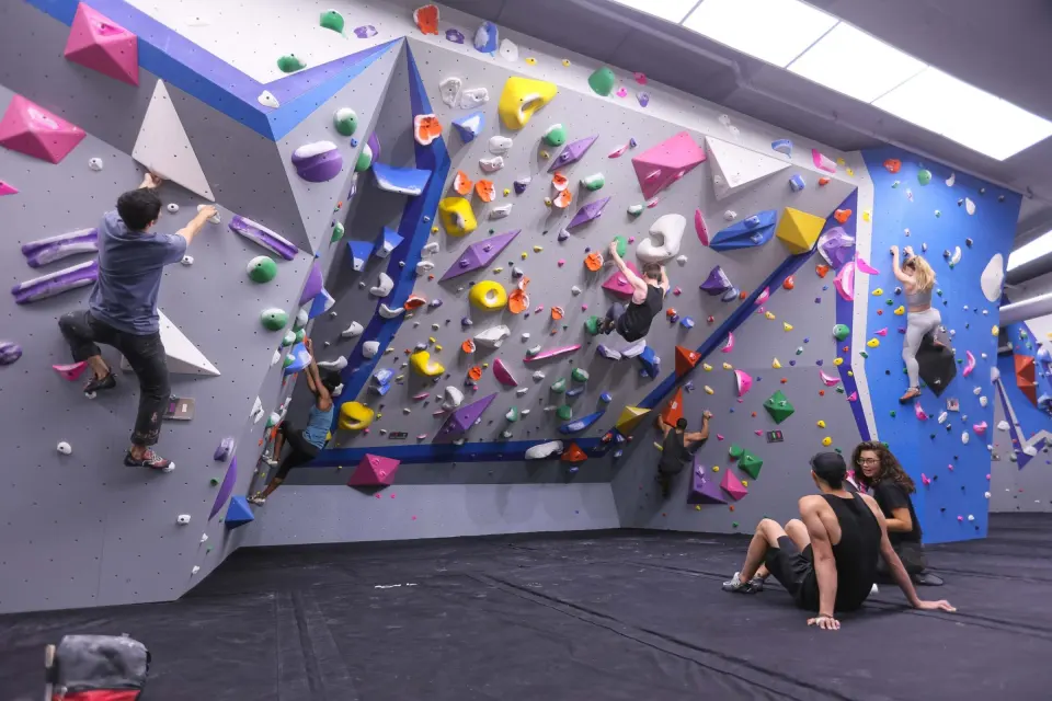 Climbers on the grey and blue bouldering walls above black matting