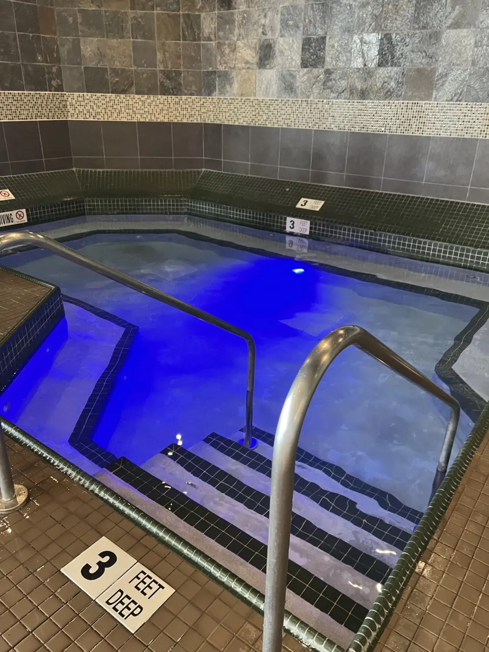Indoor whirlpool lit blue, with a handrail and tiled walls