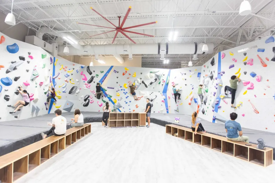 Bright bouldering hall with climbers on the walls and benches with cubbies