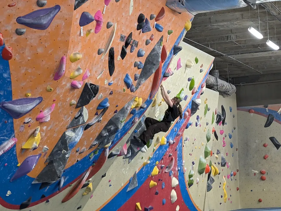 Climber on the steep orange wall with big dark volumes