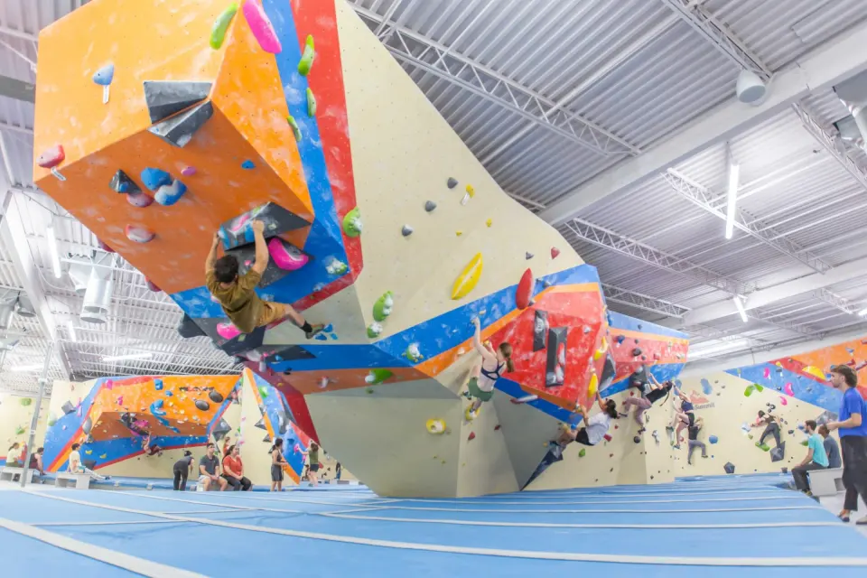 Climbers on an orange and blue overhanging boulder above blue matting