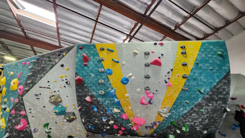 Bouldering wall striped in teal, yellow, grey and white