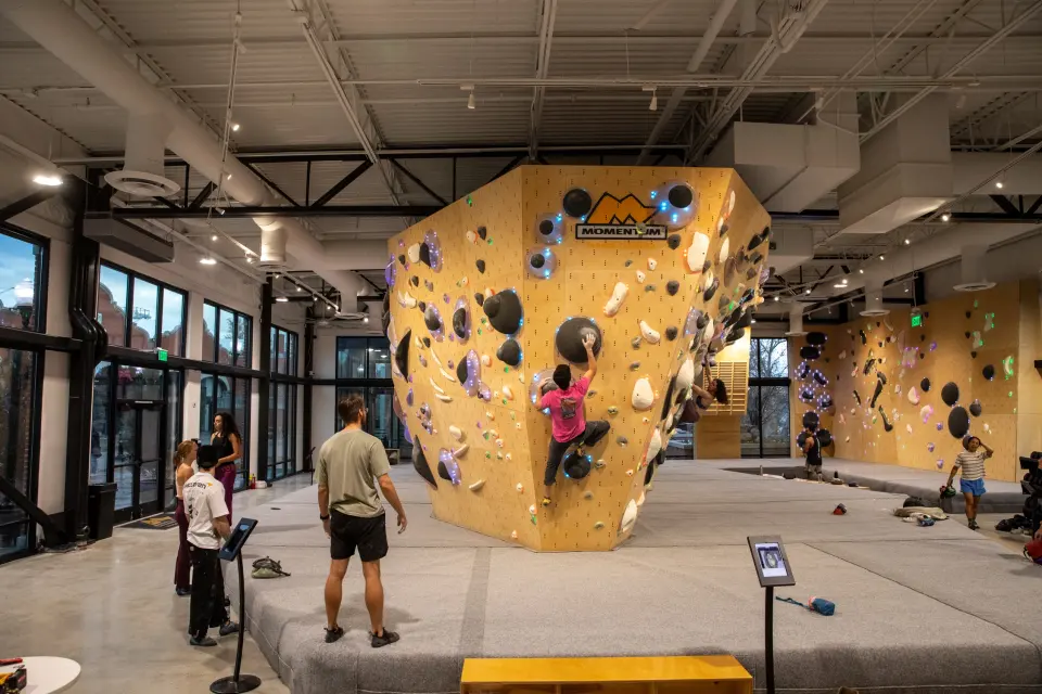 Bouldering hall with a wooden tower under the Momentum logo and big windows behind