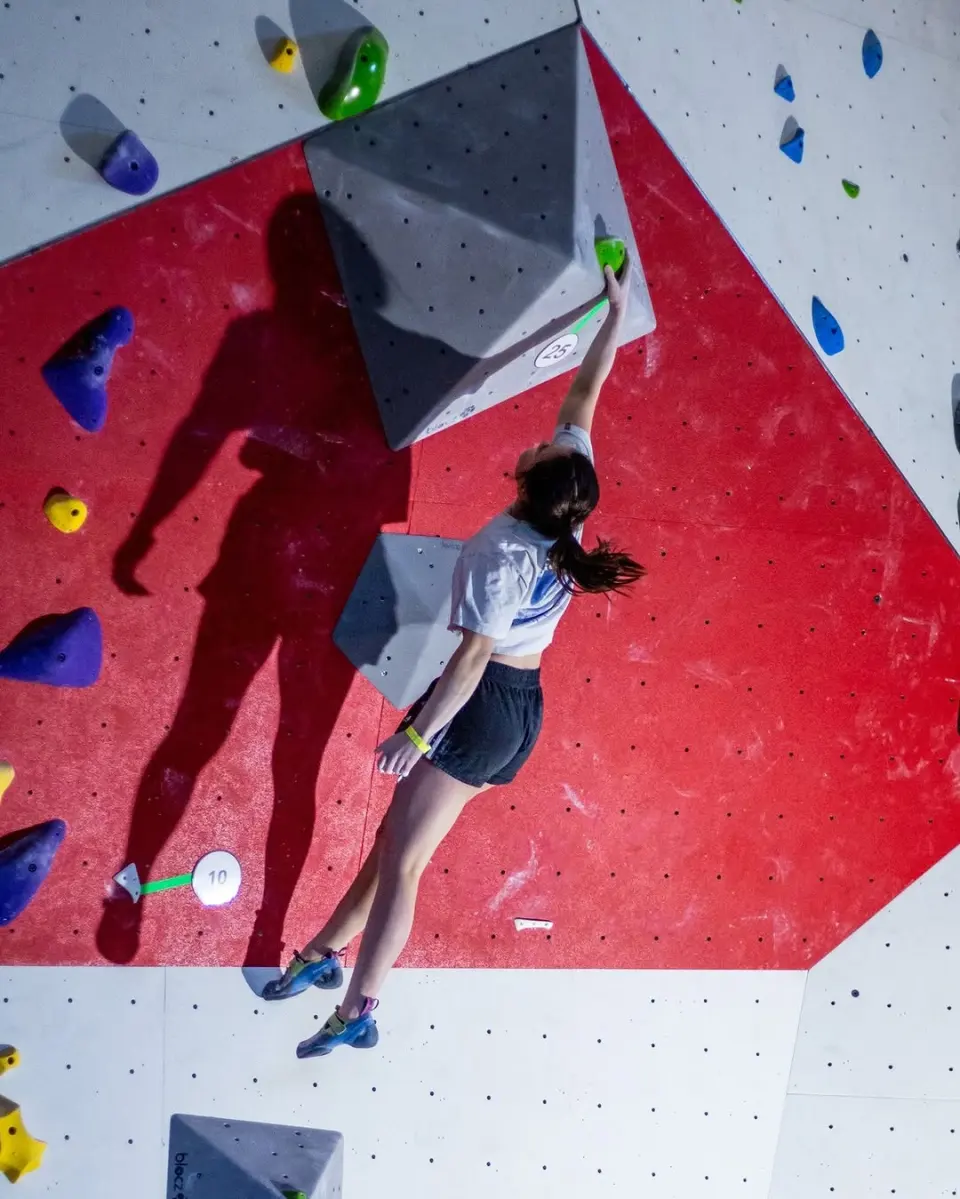 Climber reaching for a grey volume on a red and white wall