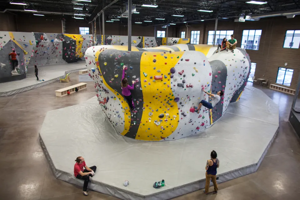 Yellow, grey and white freestanding boulder on a wide padded floor in the bouldering hall