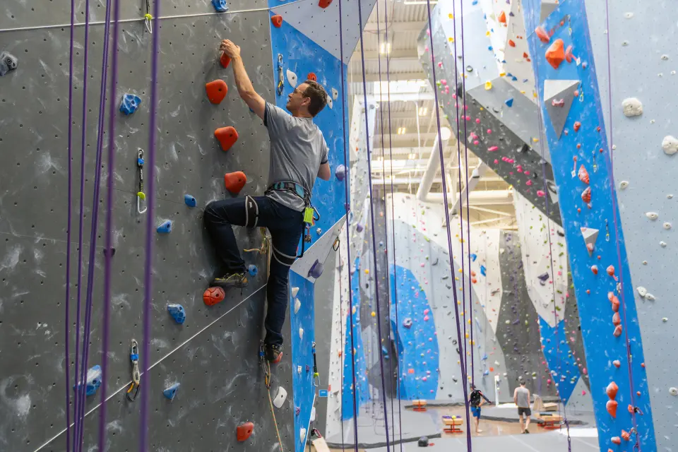Climber on a grey rope wall, with tall blue and white walls stretching behind