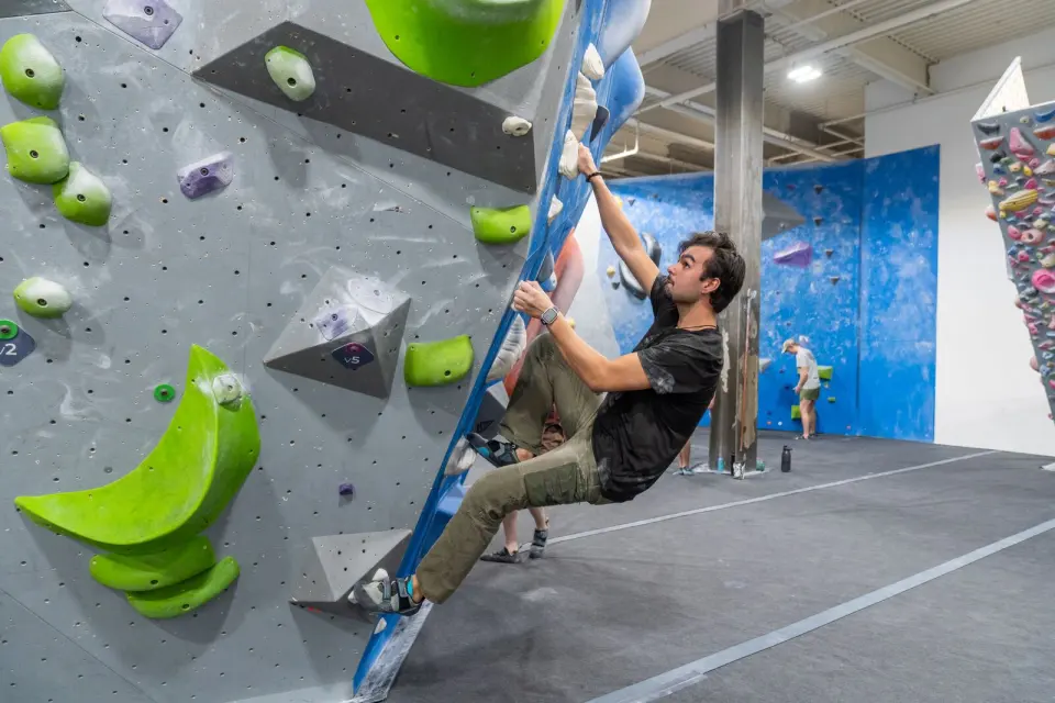 Climber on a bouldering wall with bright green volumes