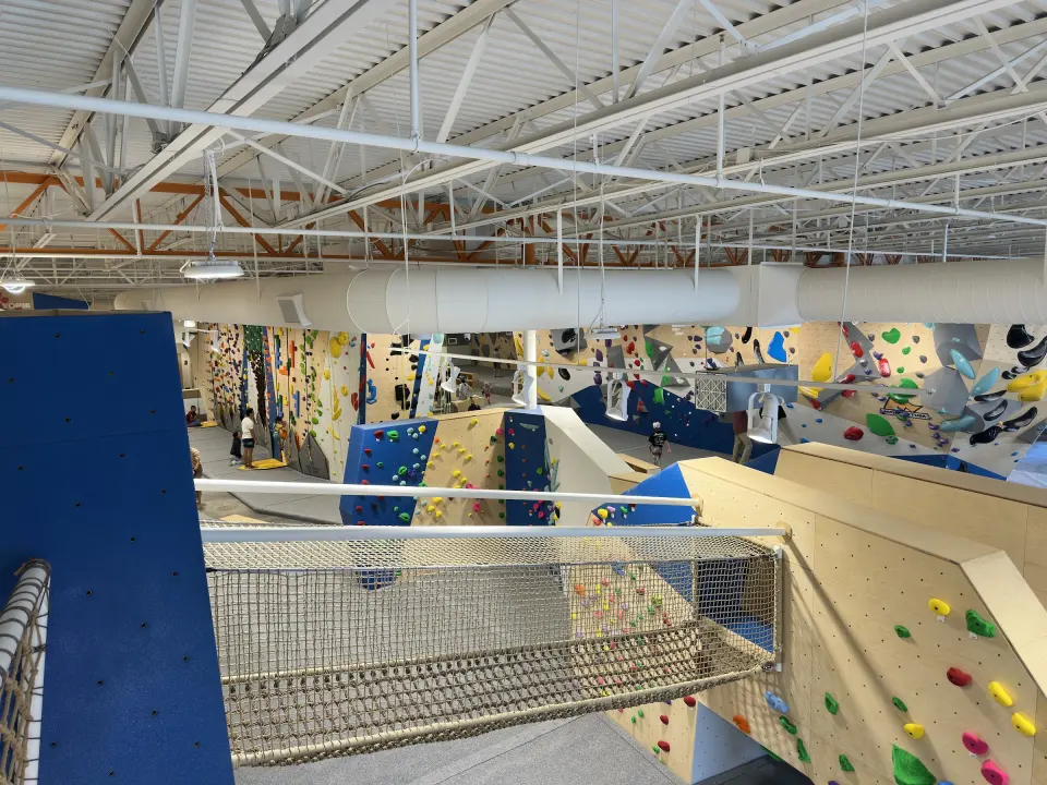 Climbing hall seen from a rope-net bridge, with auto-belay and bouldering walls beyond