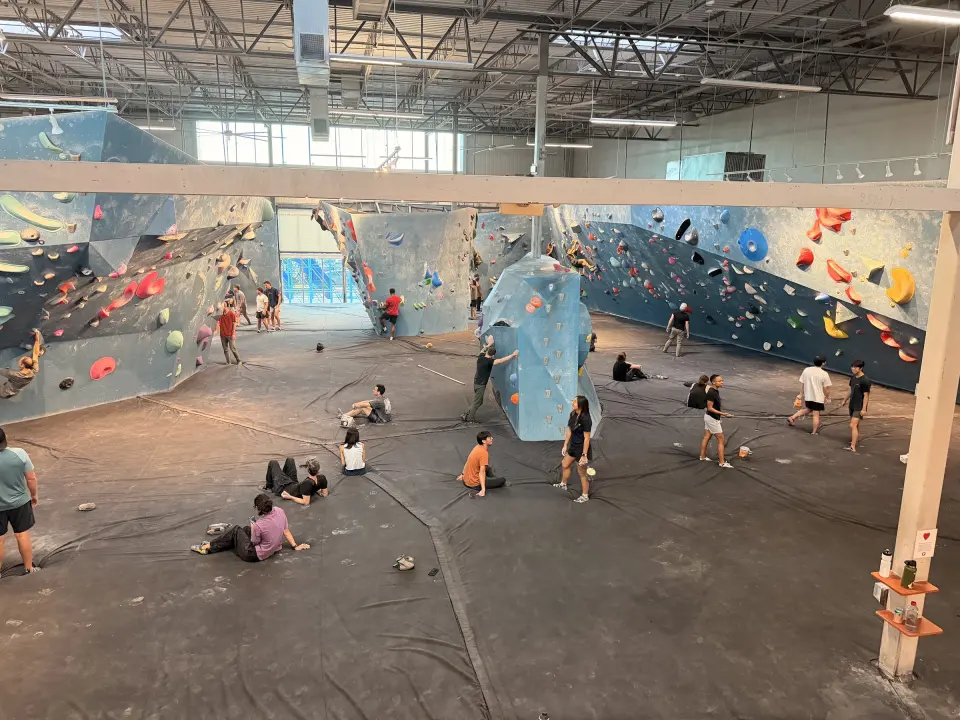 Bouldering floor seen from the mezzanine, with blue walls and freestanding boulders