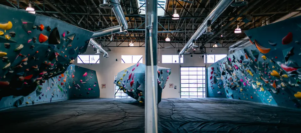 Teal bouldering walls with overhangs and volumes under the timber roof of the main hall