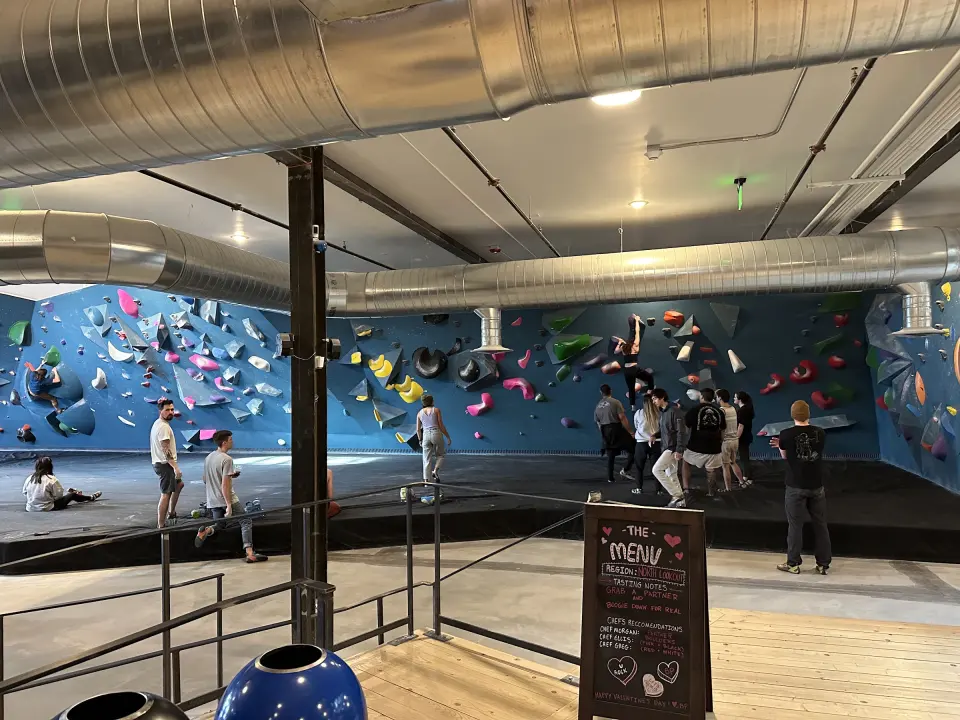 Climbers on the long teal bouldering wall, seen from the lobby