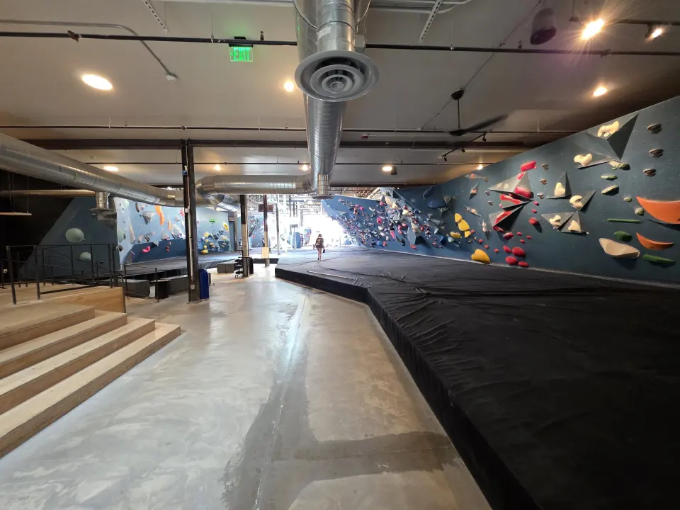 Wooden steps beside the matting along a teal bouldering wall
