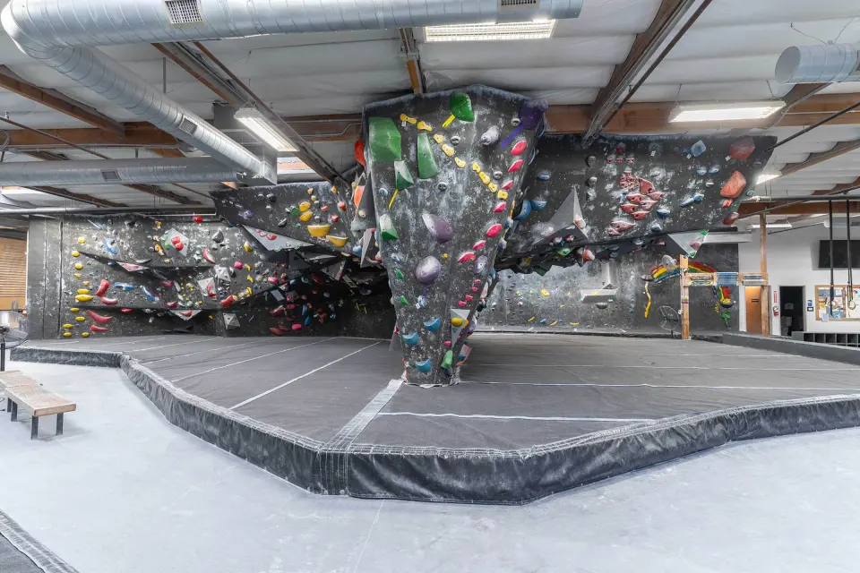 Bouldering hall with a central pillar boulder and dark walls around grey matting