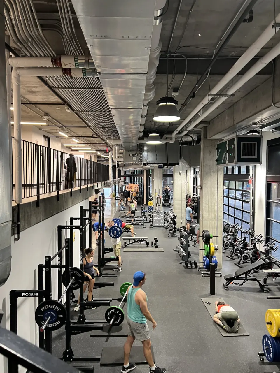 Long fitness hall with squat racks below a mezzanine walkway