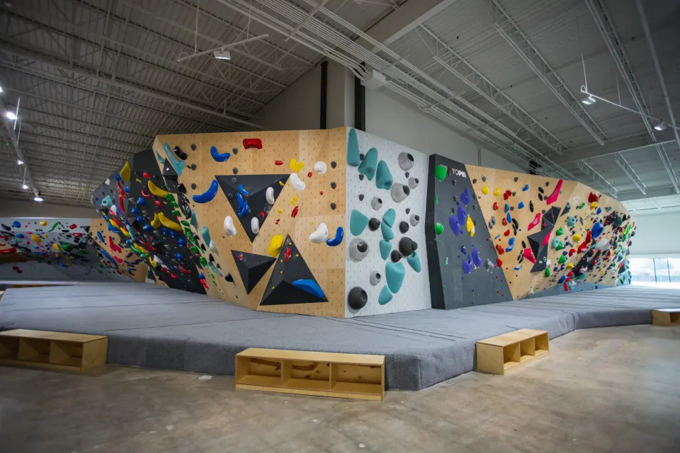 Long bouldering wall in wood and grey panels with colourful holds and volumes above deep matting