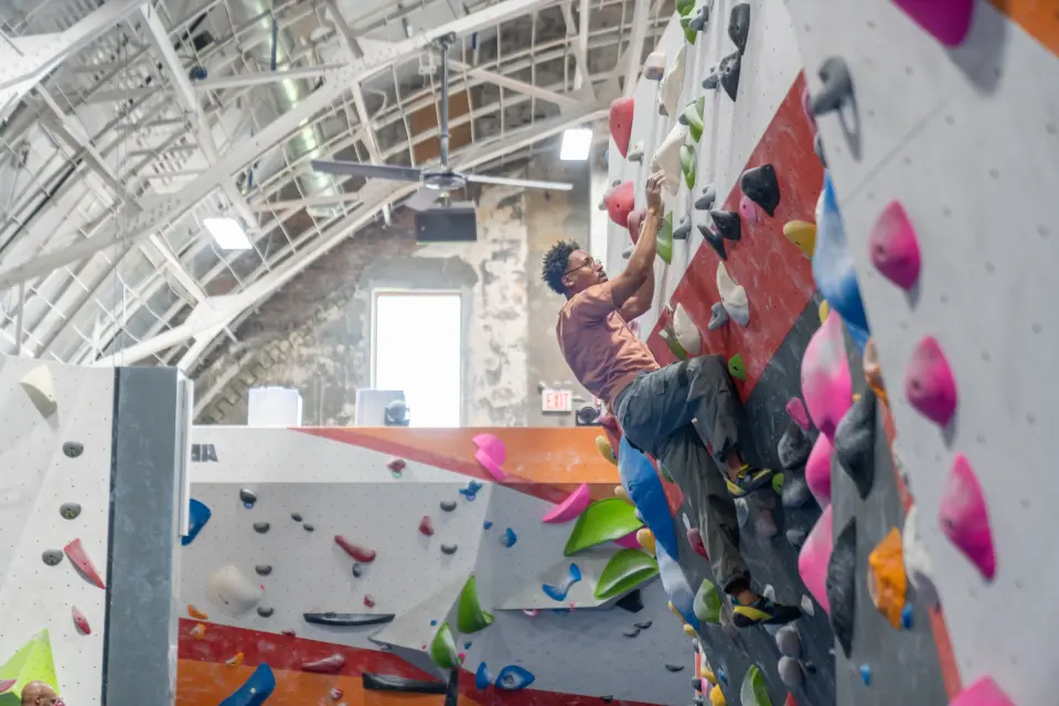 Climber reaching for pink holds below the arched roof trusses