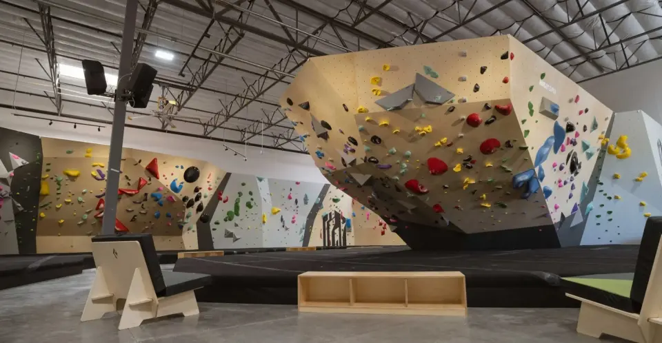 Bouldering hall with a large overhanging plywood prow above deep black matting