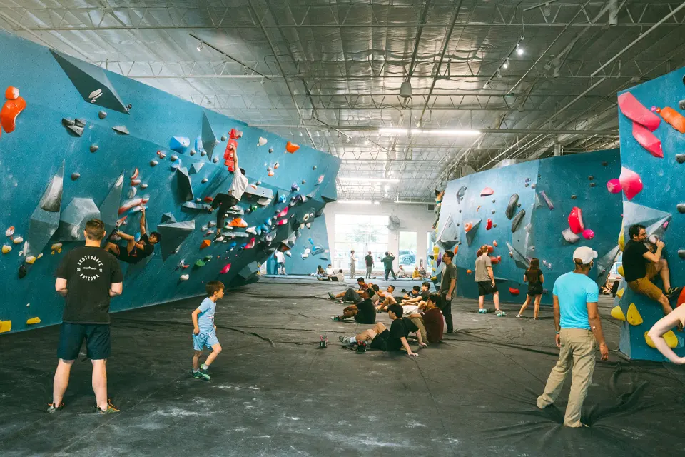 Long bouldering hall with blue walls and climbers resting on the mats