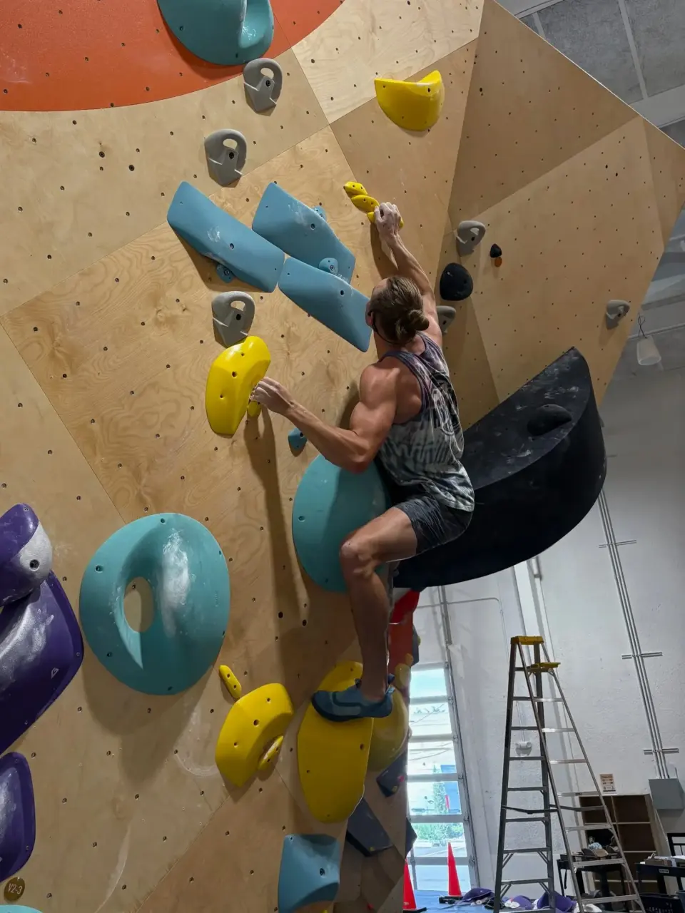 Climber on teal holds on a steep plywood bouldering wall