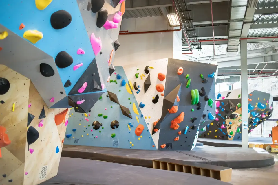 Light blue and grey bouldering walls with angled volumes under a high warehouse roof