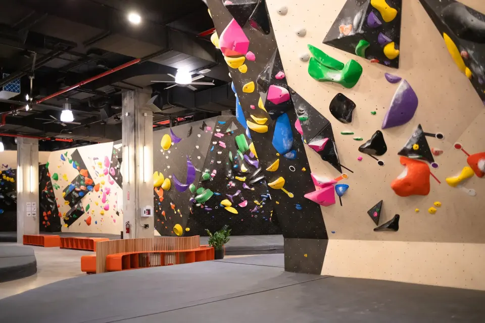 Long bouldering wall with black volumes and colourful holds above deep matting