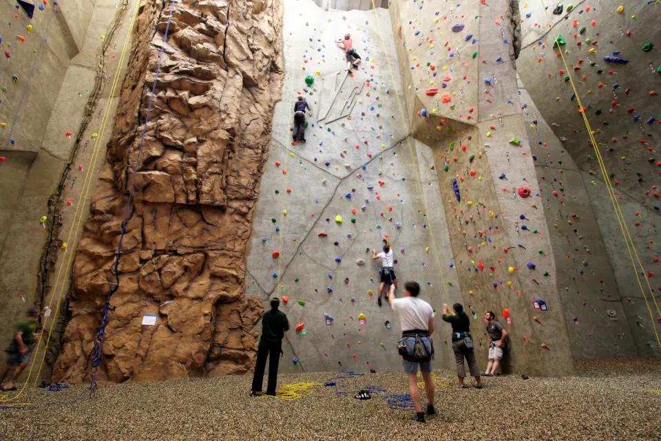 Climbers and belayers below the tall rope walls and rock-textured pillar