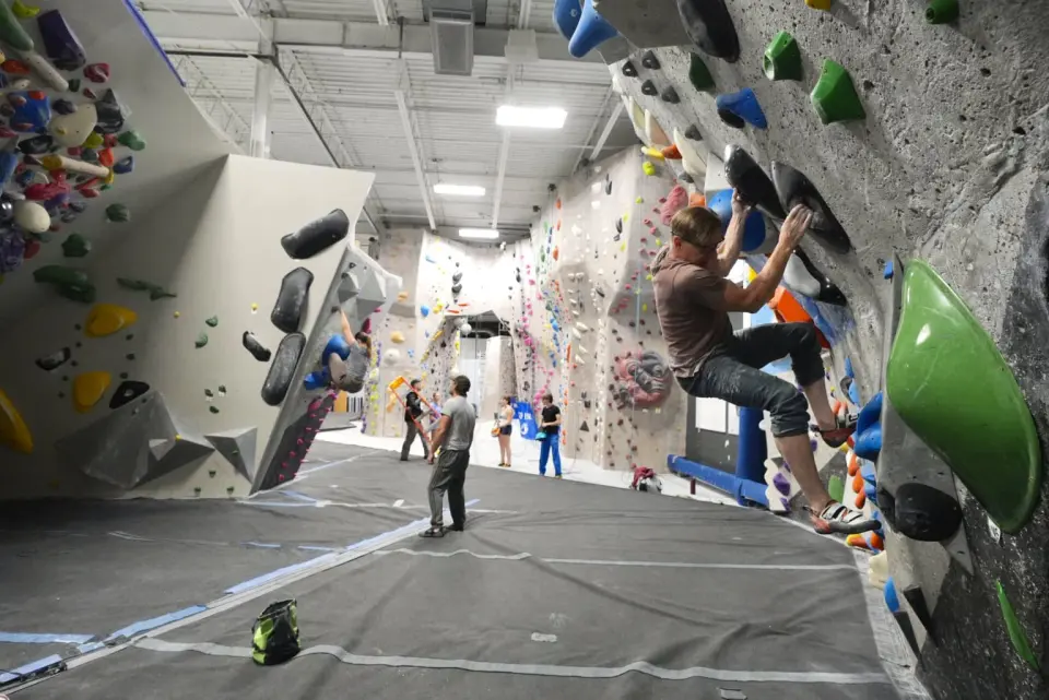 Climber on a grey overhang beside a long row of bouldering walls