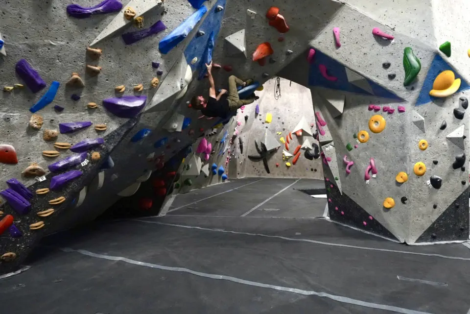 Climber under a steep bouldering arch with purple and blue holds