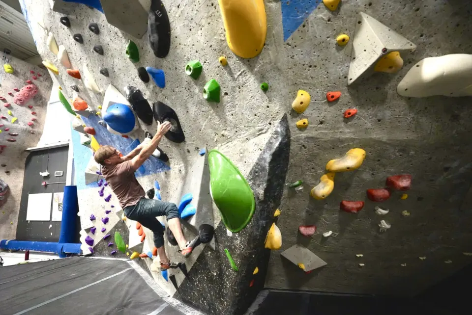 Climber reaching between big green and yellow holds on a bouldering prow