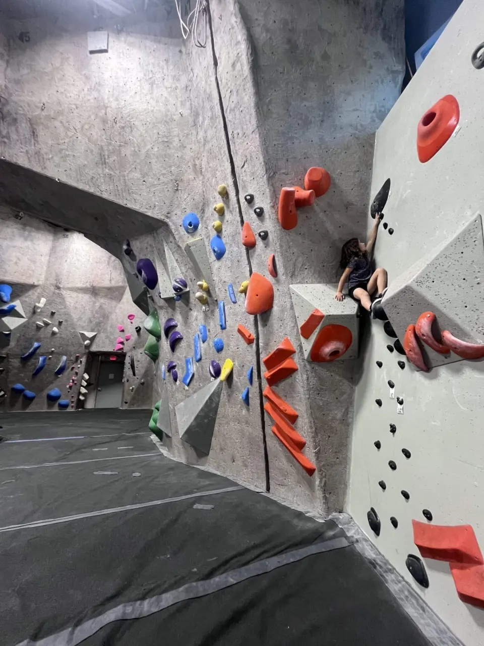 Grey wall with red volumes and a top rope beside the bouldering matting