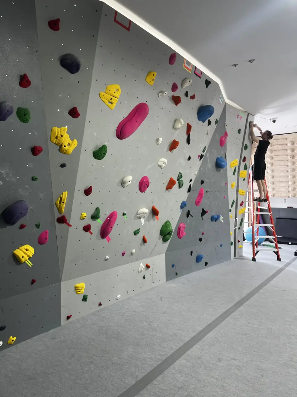 Long bouldering wall with a setter at work on a ladder